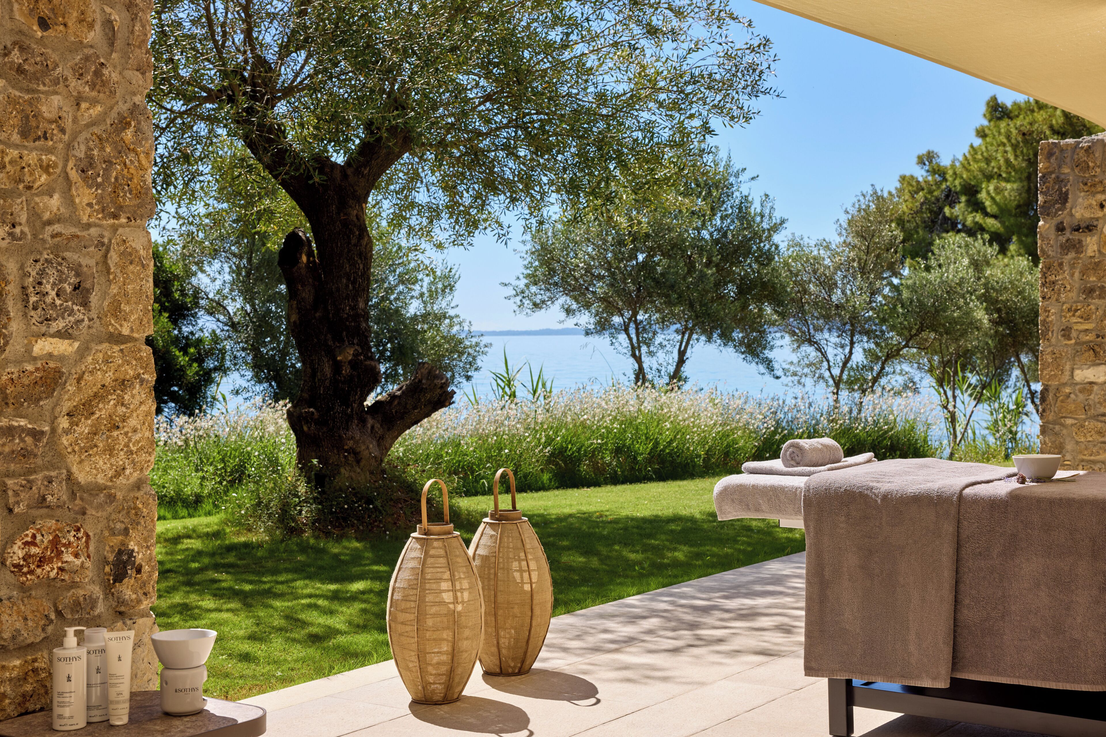 An outdoor seating area with a view of the sea, stone walls, and a tree.