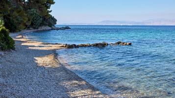 Une plage de galets bordée d’une eau d’un bleu limpide et dominée par des montagnes lointaines.