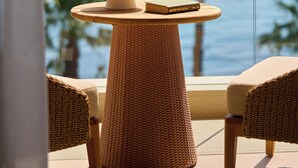 A balcony with wicker furniture, a table with a bowl and a glass, and a view of the sea and palm trees. - Avali, Mar-Bella Collection (Corfu)