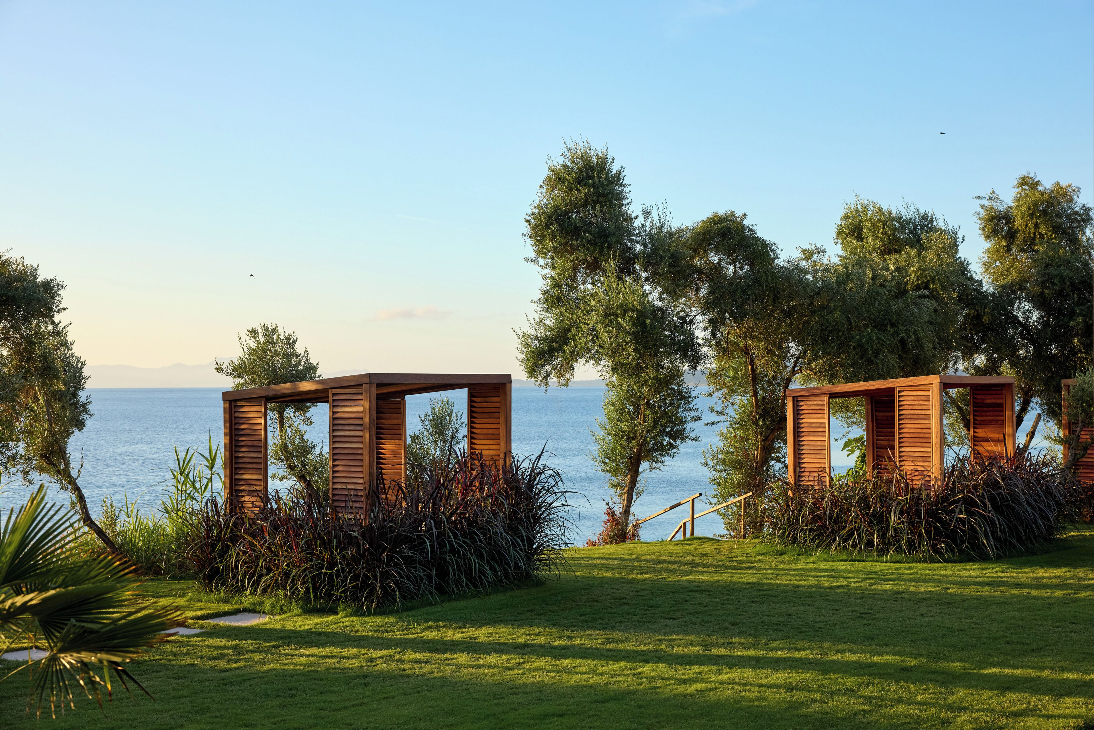 A coastal property with two wooden gazebos, a grassy lawn, and a view of the sea.