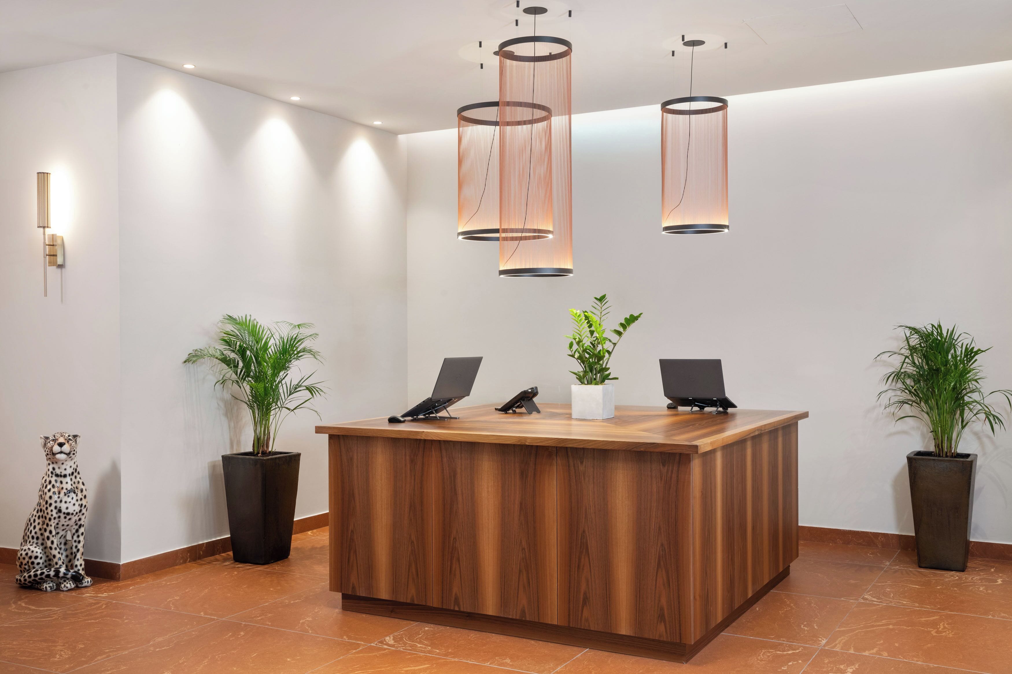 Un comptoir d’accueil avec deux ordinateurs portables, un téléphone et une plante en pot. Trois lampes suspendues sont fixées au-dessus du comptoir.