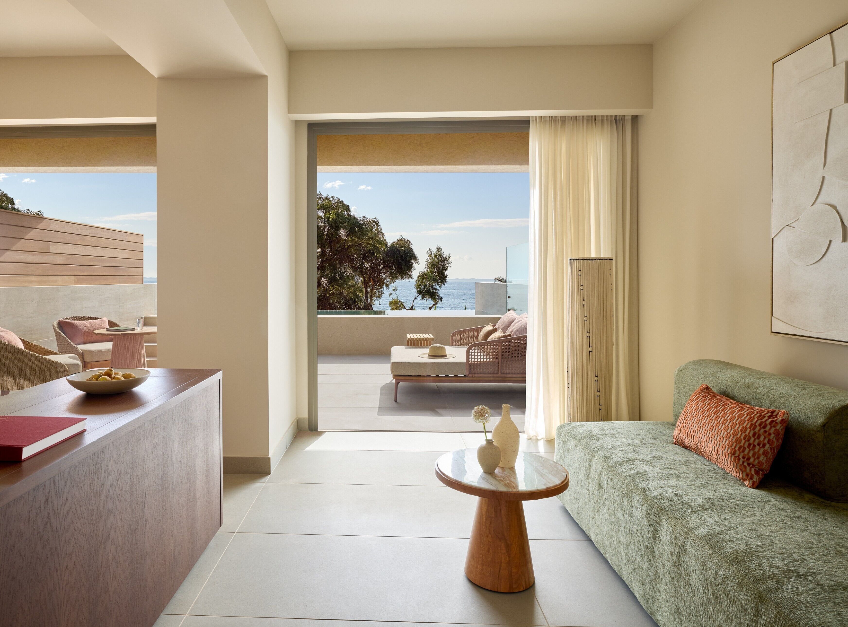 A modern hotel room with a balcony, a sofa, a dining table, and a view of the sea.