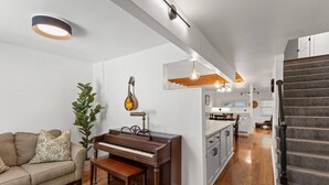 A modern living room with a piano, a couch, and a staircase leading to a kitchen area.