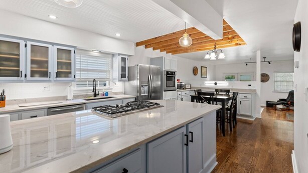 A modern kitchen with white cabinets, a central island, stainless steel appliances, and a wooden ceiling.