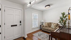 A living room with a beige sofa, a piano, a lamp, and a plant.