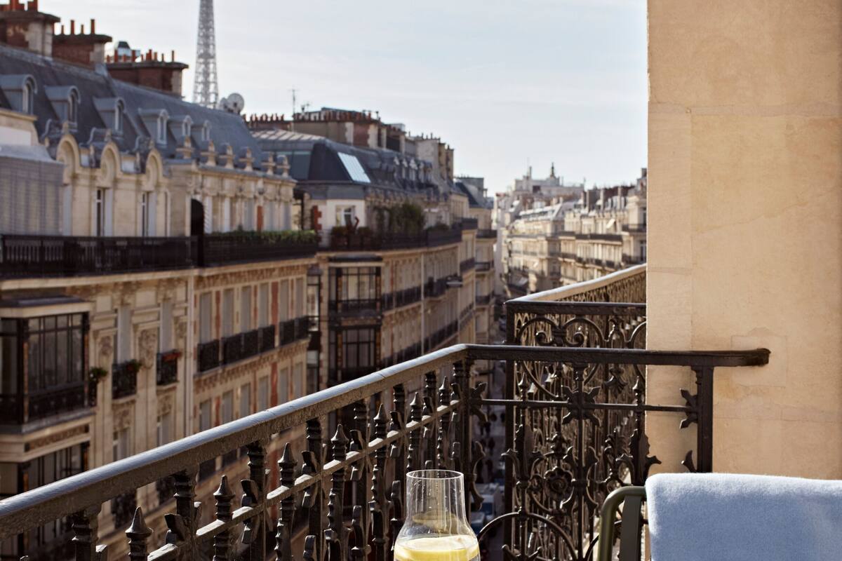 A balcony with wrought iron railings overlooking a cityscape with historic buildings and a tower.