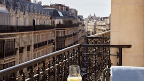 En balkon med smedejernsrækværk med udsigt over en by med historiske bygninger og et tårn.