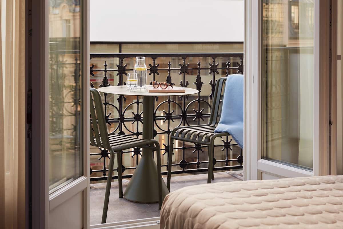 A balcony with a round table, two chairs, a small table with a bottle and glasses, and a blue towel.