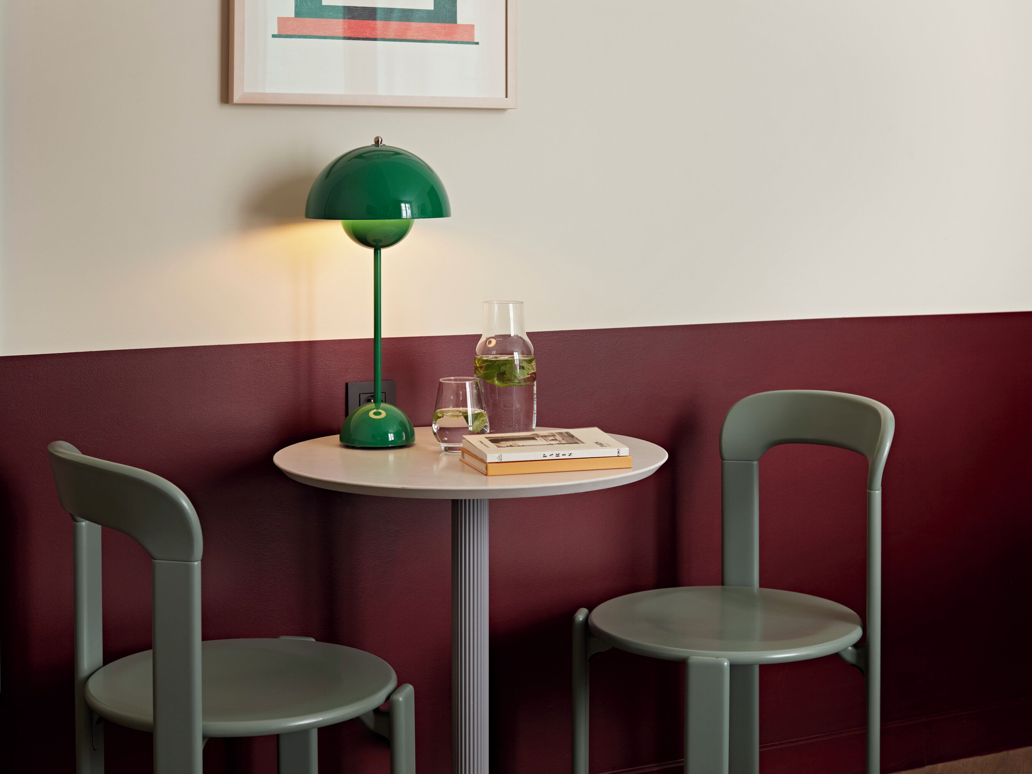A small round table with a green lamp, two chairs, a glass of water, a book, and a bottle of water.