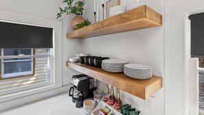 A kitchen with white walls, wooden shelves holding plates, cups, and a coffee maker. There is a window with blinds and a potted plant on the shelf. - This house is a 2 bedroom(s), 2 bathrooms, located in Frankfort, KY. (Frankfort)