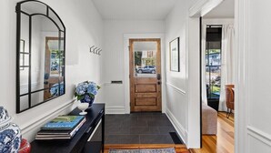 A hallway with a wooden door, a mirror, a vase with flowers, and a book on a console table. - This house is a 2 bedroom(s), 2 bathrooms, located in Frankfort, KY. (Frankfort)