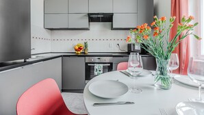 Et moderne køkken med lysegrå skabe, en indbygget ovn og et spiseområde med et hvidt bord dækket til to.