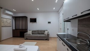 A modern hotel room with a bed, a sofa, a kitchen area with a sink, and a flat-screen TV mounted on the wall. - Star&Sea Saranda (Sarandë)