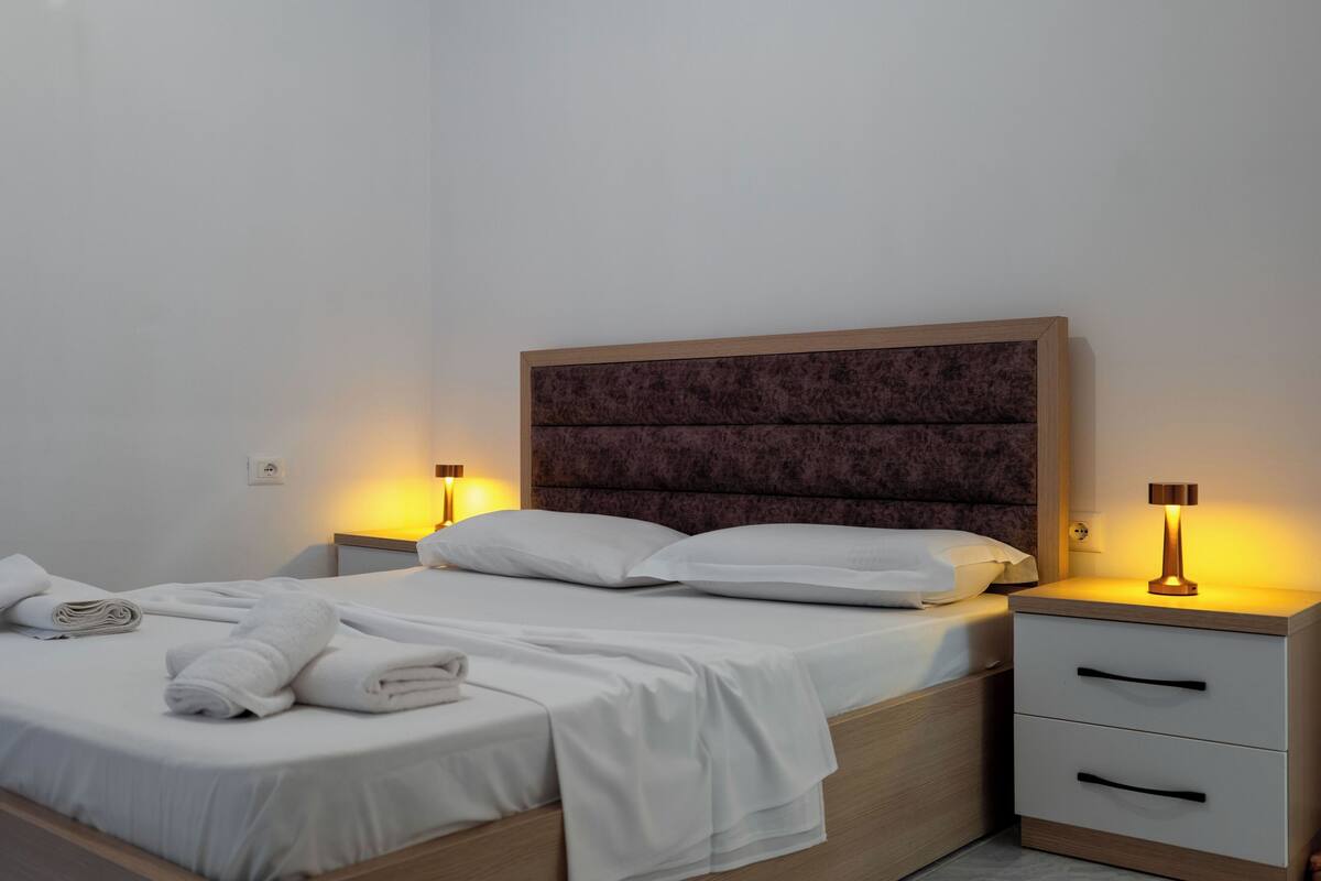 Un lit bien fait, avec du linge de lit blanc, deux tables de chevet avec des lampes et une tête de lit en bois.