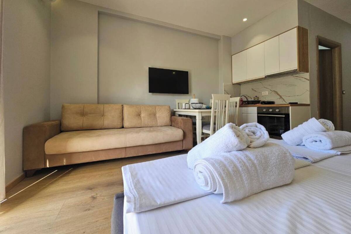 Une chambre d’hôtel avec un canapé, un lit avec des serviettes pliées, une télévision et une kitchenette.