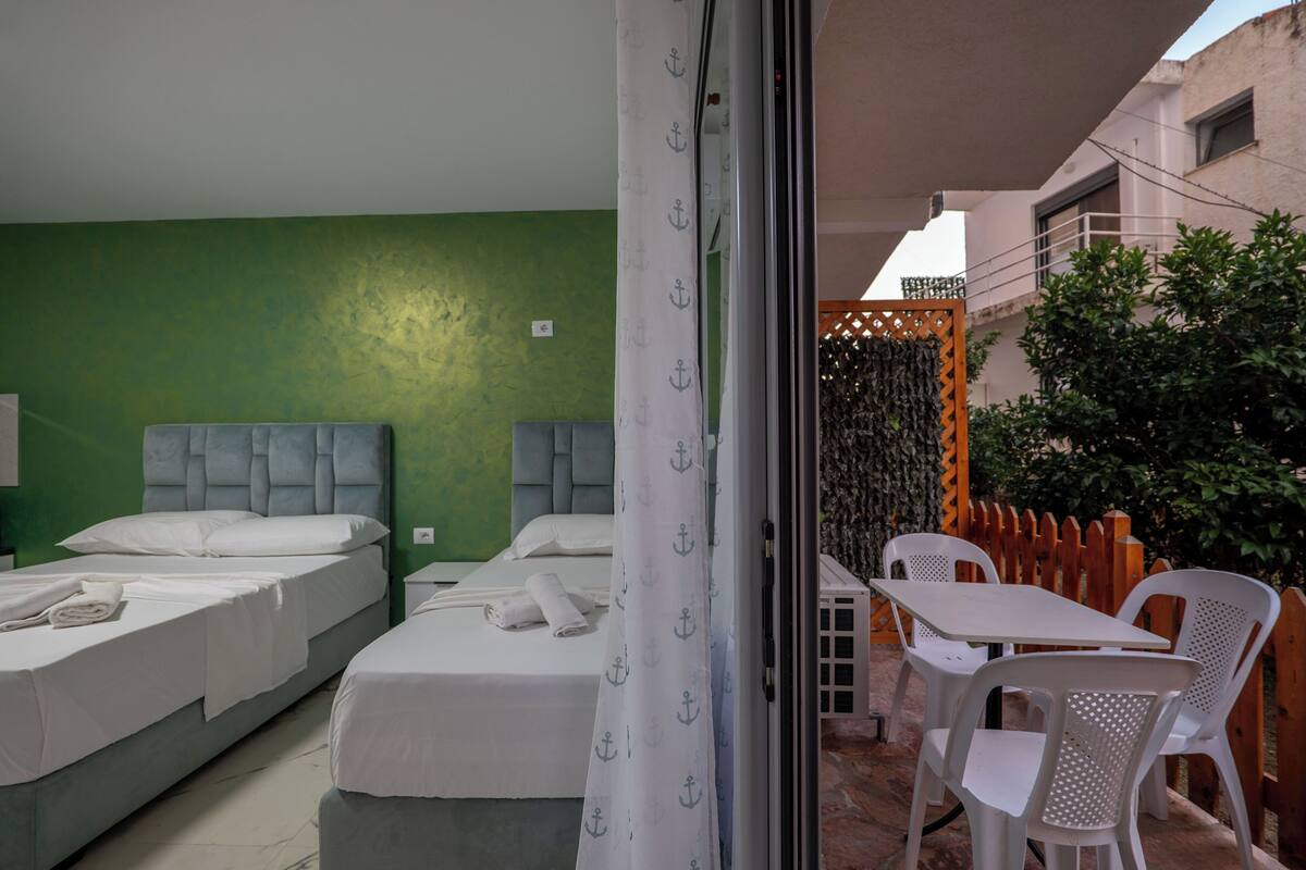 Une chambre avec deux lits, une table et des chaises, un mur vert et une vue sur l’extérieur.