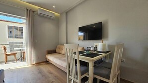 A modern living room with a sofa, a dining table with chairs, a flat-screen TV mounted on the wall, and an air conditioning unit. - Star&Sea Saranda (Sarandë)