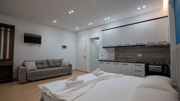 A modern bedroom with a bed, a sofa, a TV, and a kitchenette. - Star&Sea Saranda (Sarandë)