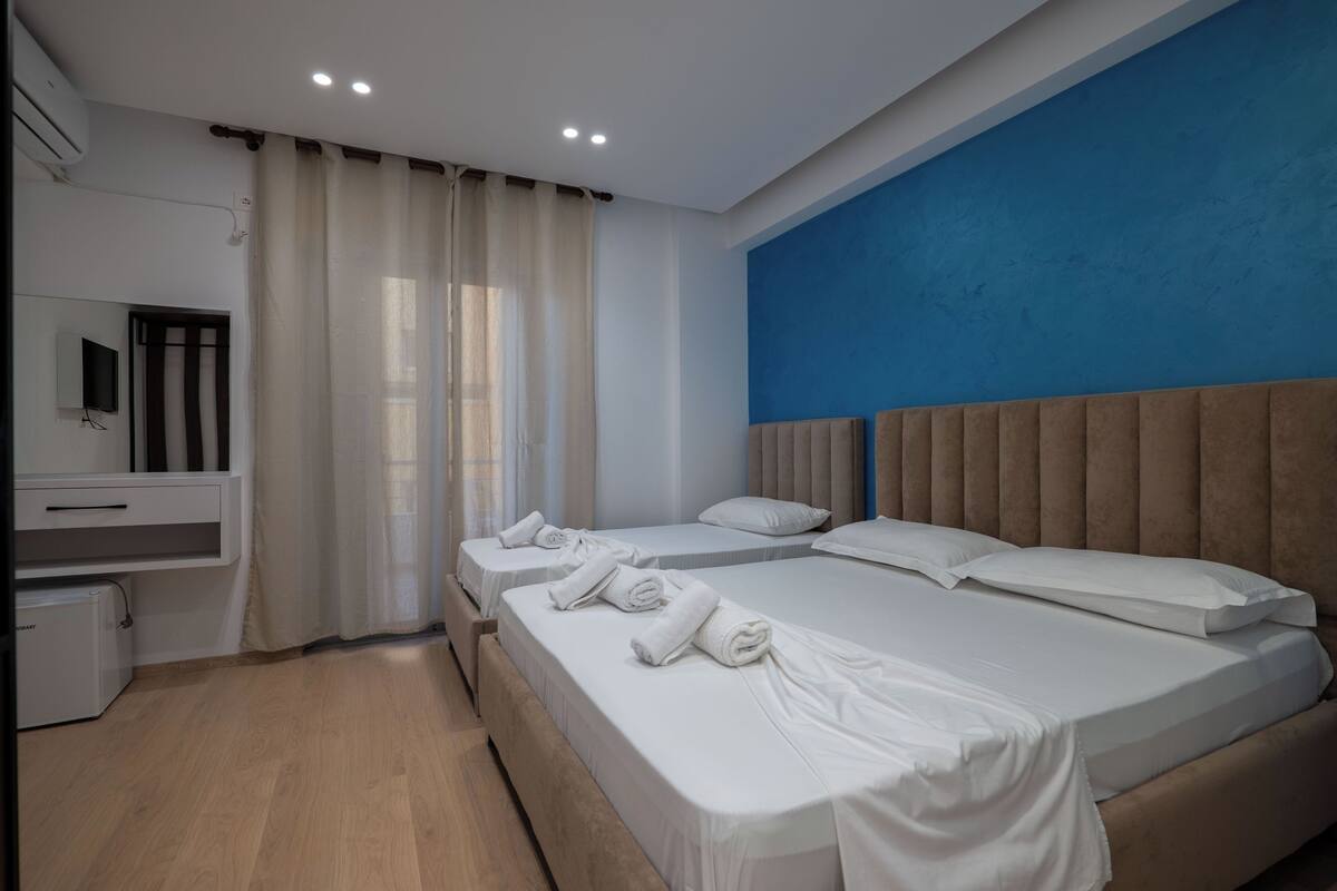 Une chambre d’hôtel avec un grand lit, deux petits lits, un bureau et une télévision.