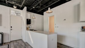 A modern kitchen with white cabinetry, a central island, pendant lighting, and a visible door leading to another room. - Studio 3 mins from OU — a semester base without signing a 12-month lease (Norman)