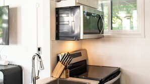 A modern kitchen with a stainless steel sink, black stove, white cabinets, and a hanging pendant light. - Studio 3 mins from OU — a semester base without signing a 12-month lease (Norman)
