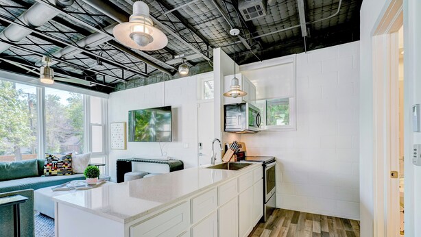 A modern kitchen with white cabinetry, a large island, and a dining area with a green sofa. - Studio 3 mins from OU — a semester base without signing a 12-month lease (Norman)
