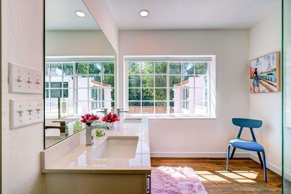 A modern bathroom with a large mirror, a sink, and a window.
