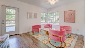 Ein Zimmer mit großem Fenster, einer Kristallleuchtre und rosa Stühlen um einen kleinen Tisch.
