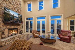 A spacious living room with a stone fireplace, a large flat-screen TV, and a glass coffee table.