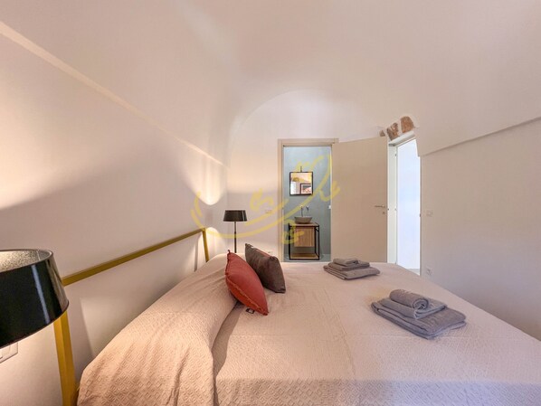 A bedroom with a bed, pillows, a lamp, a sink, and towels. - TD Trullo Morena Charming Trullo Stunning Sunsets (Monopoli)