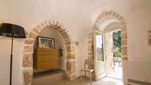 Une pièce avec une arche en pierre, une commode jaune, une chaise blanche et une lampe.