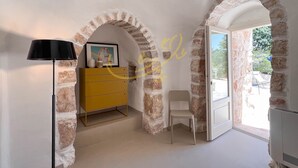 Une pièce aux murs en briques apparentes, avec une commode jaune, un tableau encadré, un lampadaire noir et une chaise blanche.