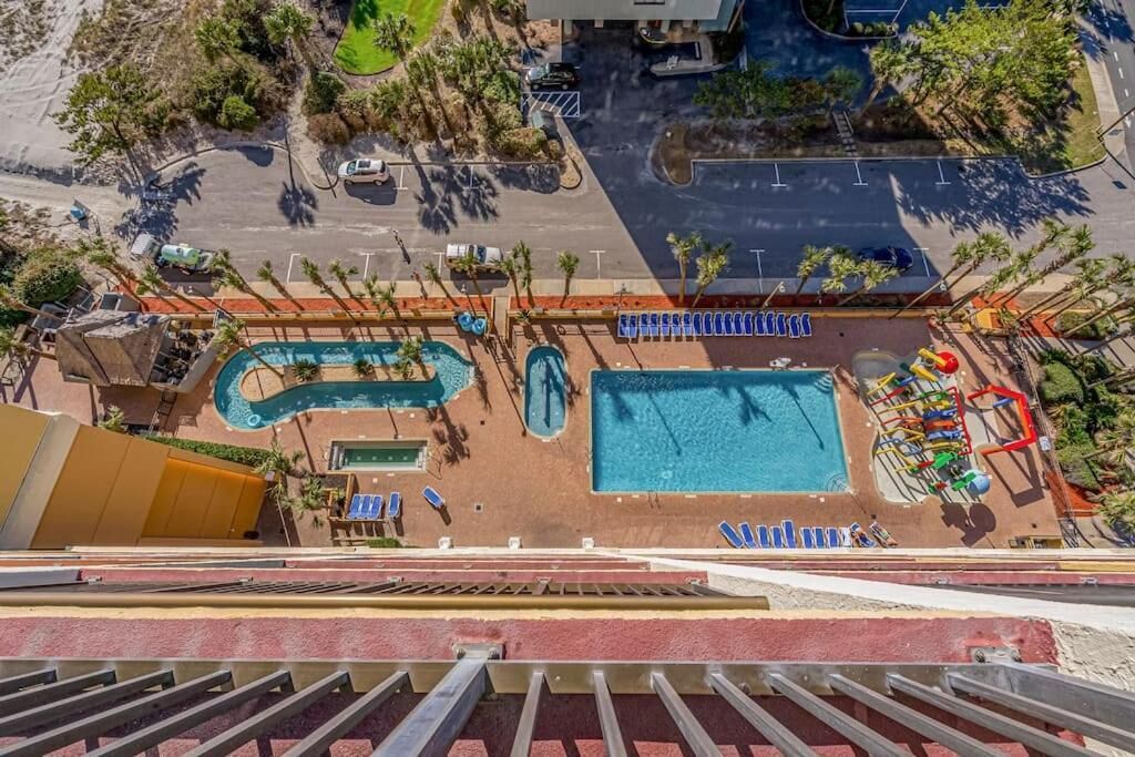 An aerial view of a hotel with a swimming pool, sun loungers, and a children's play area.