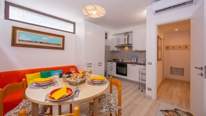 A modern kitchen with white cabinets, a built-in oven, and a dining area with a round table set for four. - Casa Angerin 1 in Alassio (Alassio)