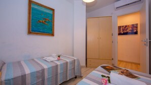 A bedroom with two beds, a painting of swimmers, a wooden wardrobe, and an air conditioning unit. - Casa Angerin 1 in Alassio (Alassio)