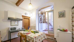 Une cuisine équipée d’une table à manger pour deux personnes, d’un four à micro-ondes, d’un réfrigérateur et d’une porte en bois donnant sur un escalier.