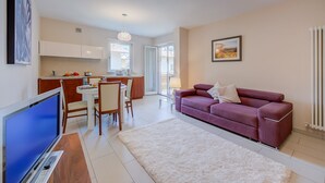 A modern living room with a TV, a purple sofa, and a dining area with chairs and a table. - Casa Margherita in Riva del Garda (Riva del Garda)