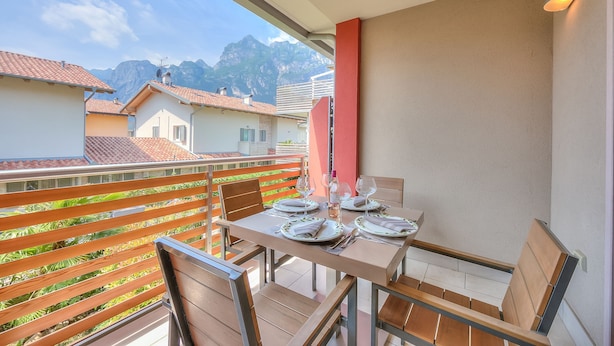 A balcony with a table set for dining, chairs, and a view of mountains. - Casa Margherita in Riva del Garda (Riva del Garda)