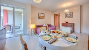 A modern living room with a dining area, featuring a round table set with plates, cups, and a fruit bowl. - Casa Margherita in Riva del Garda (Riva del Garda)