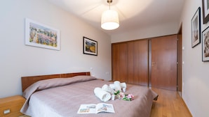 A neatly made bed with towels and a magazine, wooden wardrobe, and a painting on the wall. - Casa Margherita in Riva del Garda (Riva del Garda)
