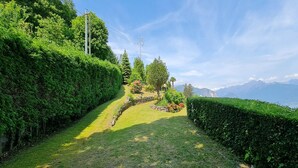 Een aangelegde tuin met een pad van stenen, keurig bijgesnoeide hagen en uitzicht op verre bergen.
