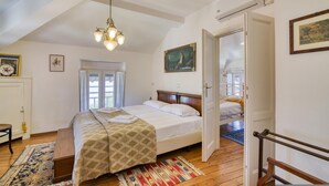 Een slaapkamer met een bed, een houten bankje, een kamerkleed met patroon en een kroonluchter.