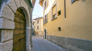 A narrow alleyway with stone walls and a wooden door, leading to a building with a yellow facade and a small window. - Sergio Il Gufo - Orange in Historic Cente (Toscolano Maderno)