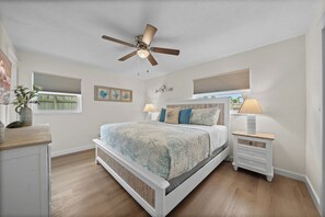 A bedroom with a bed, two bedside tables with lamps, a ceiling fan, and a window with blinds. - Island Oasis with Heated Pool, Putt Putt Course, Tiki Bar, and Beach Gear! (Merritt Island)