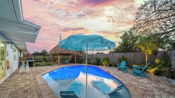 A backyard with a swimming pool, lounge chairs, and a wooden fence. - Island Oasis with Heated Pool, Putt Putt Course, Tiki Bar, and Beach Gear! (Merritt Island)