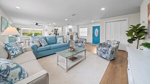 A modern living room with a blue sofa, a patterned armchair, and a coffee table. - Island Oasis with Heated Pool, Putt Putt Course, Tiki Bar, and Beach Gear! (Merritt Island)