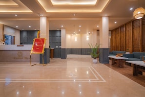 Een hotel lobby met een receptiebalie, een zithoek en een grote kamerplant.