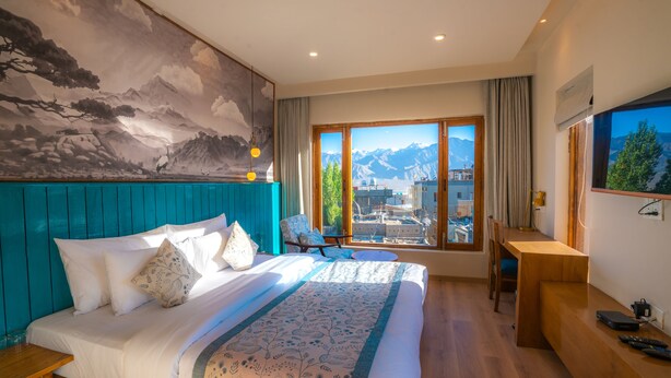Un dormitorio con una cama grande, un escritorio y vistas a las montañas a través de la ventana.