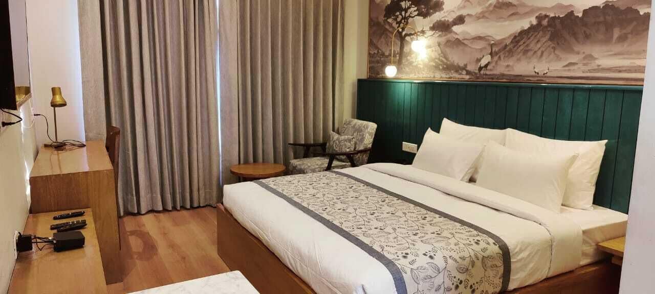 A hotel room with a large bed, a desk with a lamp, a chair, and a painting on the wall.