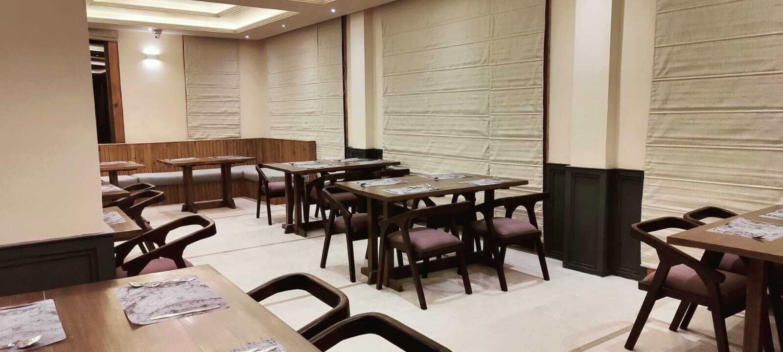 A hotel dining area with multiple tables and chairs, wooden paneling on the walls, and a neutral color scheme.